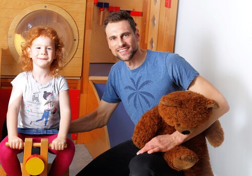 Kindergartenpädagoge mit einem Kind vor einer Rutsche im Kindergarten Kindergartenpädagoge mit einem Kind vor einer Rutsche im Kindergarten