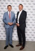 Landesrat Markus Achleitner und Peter Leitner stehen nebeneinander vor einer Fotowand mit vielen Firmenlogos des Betriebes