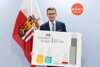 Wirtschafts-Landesrat Markus Achleitner hält eine Grafik zum Standortbudget des Landes Oberösterreich; im Hintergrund die Oberösterreich-Fahne.