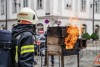 Feuerwehr-Einsatzkraft in voller Montur vor einem Ofen, aus dem Flammen steigen