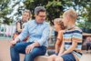 Landesrat Mag. Michael Lindner auf einem Spielplatz sitzend im Gespräch mit drei Kindern