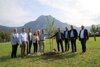 Eine Gruppe von neun Personen, unter ihnen Landeshauptmann-Stellvertreter Dr. Manfred Haimbuchner, steht auf einer Wiese bei einem frisch eingepflanztem Bäumchen, im Hintergrund hoher Berg