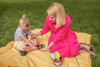Gesundheitsreferentin LH-Stv.in Mag.a Christine Haberlander sitzt mit einem Kind auf einer Decke in einer Wiese; Sie cremt das Kind mit Sonnencreme ein.