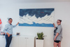 Landesrat Mag. Michael Lindner und eine Jugendliche stehen links und rechts von einem Bild, das an der Wand hängt und stilisiert das Meer, Berge und Himmel zeigt