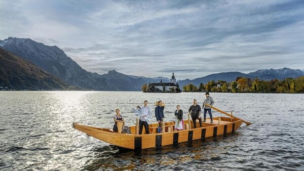 Sechs Personen auf einer großen Zille auf dem Traunsee, im Hintergrund Schloss Ort, Berge