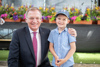 Landeshauptmann Mag. Thomas Stelzer sitzend mit einem Kind, im Hintergrund bunte Blumenkästen