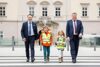 LH-Stv. Manfred Haimbuchner und LR Günther Steinkellner mit zwei Kindern mit Schultasche und Schutzweste beim Überqueren des Zebrastreifens vor dem Linzer Landhaus.