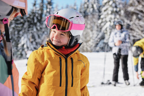 Ein gut gelauntes Mädchen in Skibekleidung in einer Skiregion.