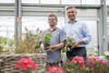 Thomas Fischer und Landesrat Dr. Wolfgang Hattmannsdorfer, jeweils mit einem Blumentopf in Händen, stehen nebeneinander in der Verkaufshalle eines Pflanzenmarktes