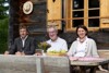 Johann Feßl, Robert Türkis und Landesrätin Michaela Langer-Weninger sitzen nebeneinander an einem Tisch direkt vor einer Almhütte
