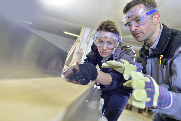 Lehrherr und Lehrling in Schutzkleidung an einer Hobelmaschine