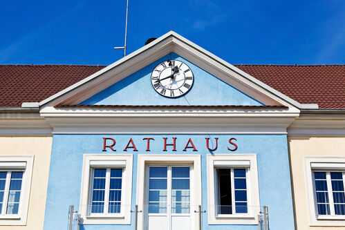 Symbolisch ist ein Rathaus mit Uhr dargestellt