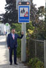 Landesrat Mag. Günther Steinkellner steht auf einem Gehweg und deutet auf das Verkehrsschild Achtung Schulweg
