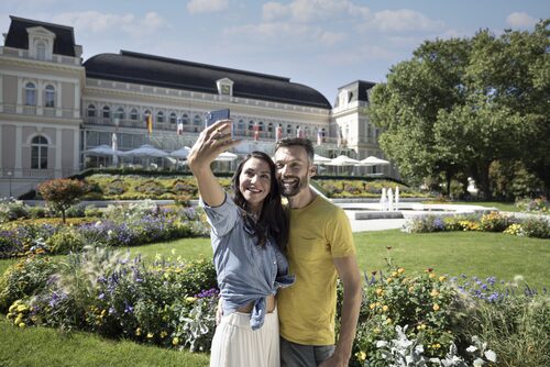Ein Paar macht ein Selfie in einem Park vor einem Schloss – der Kaiservilla in Bad Ischl