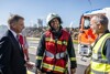 Landeshauptmann Mag. Thomas Stelzer, ein Feuerwehrmann und ein Mann mit Sicherheitsweste im Gespräch auf einem Betriebsgelände, im Hintergrund Einsatzfahrzeug, Industriegebäude