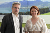 Dr. Franz Sinabell und Landesrätin Michaela Langer-Weninger stehen nebeneinander vor einer Fotowand, auf der eine Landschaft mit See, Wald und Bergen abgebildet ist