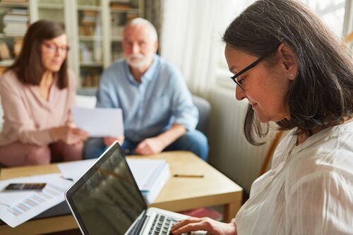 Beratungssituation, Sozialarbeiterin am Laptop, im Hintergrund eine Frau und ein Mann, auf dem Tisch Papiere