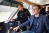 Landesrat Stefan Kaineder sitzend am Steuer eines Bootes, neben ihm ein Polizist in Uniform.