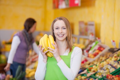 Junge Frau mit Bananen in Händen in der Obstabteilung eines Supermarktes