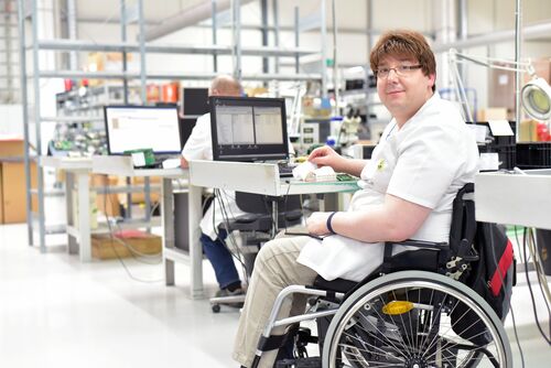 Person im Rollstuhl in einer Fertigungshalle arbeitet an einem Computer