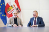 Prof. Mag. Dr. Alfred Weidinger und Landeshauptmann Mag. Thomas Stelzer sitzen nebeneinander an einem Tisch, im Hintergrund EU- und Oberösterreich-Fahne