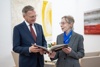 Landeshauptmann Mag. Thomas Stelzer und Dr.in Anna Mitgutsch stehen nebeneinander im Gespräch, gemeinsam halten sie ein Buch