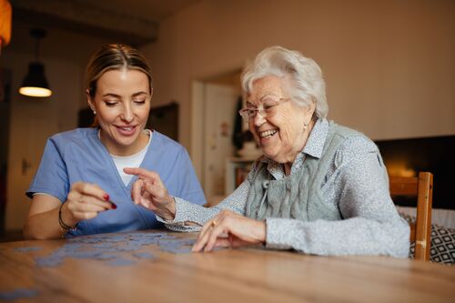 Pflegefachkraft und ältere Dame bauen zusammen ein Puzzle