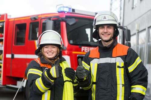 Feuerwehrfrau und Feuerwehrmann stehen vor einem Feuerwehrauto