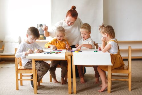 Kindergartenpädagogin unterstützt Kinder beim Malen